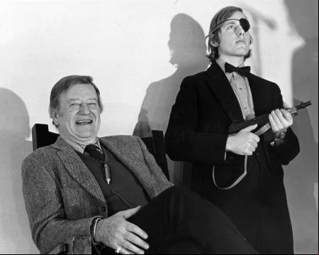John Wayne durante su intervención en el Harvard Square Theatre. Los de Lampoon iban con esmoquin y rifles de plástico.