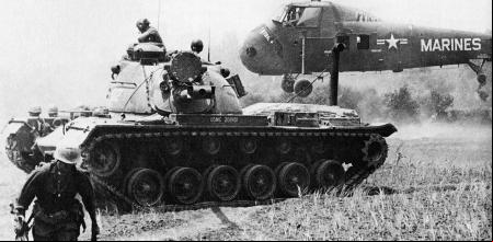 Un helicóptero MAG-16 evacua a los heridos, mientras un tanque Marine M48 Patton hace guardia.